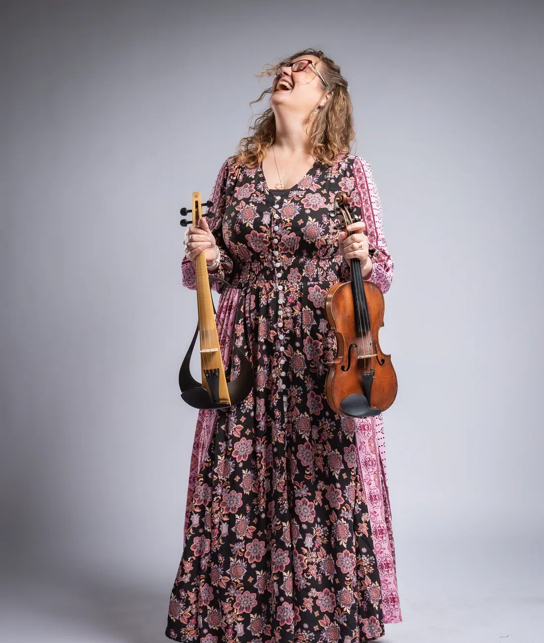Sarah Ballard laughing, holding her violin and electric violin